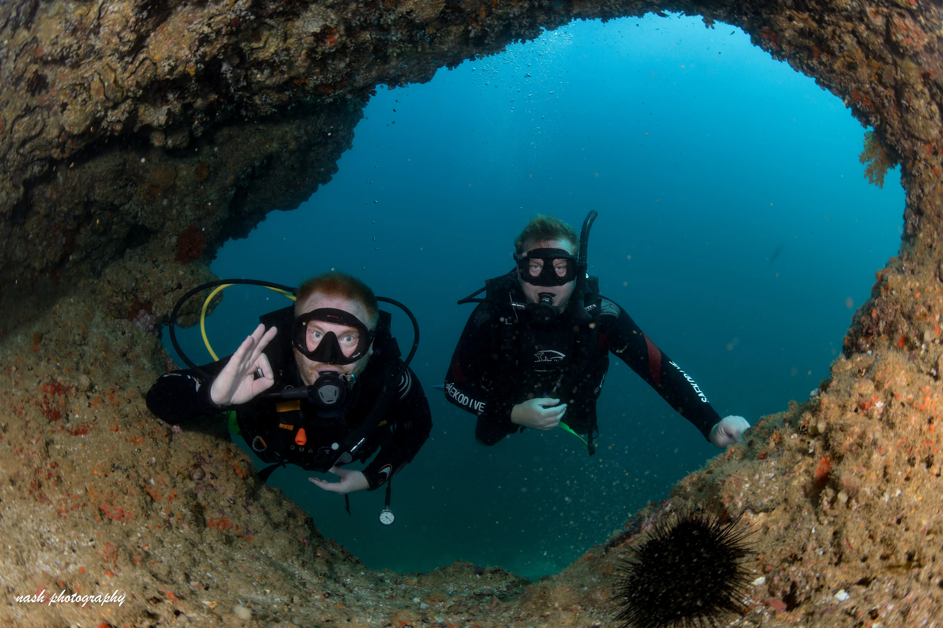 Two divers giving the OK sign in a reef arch