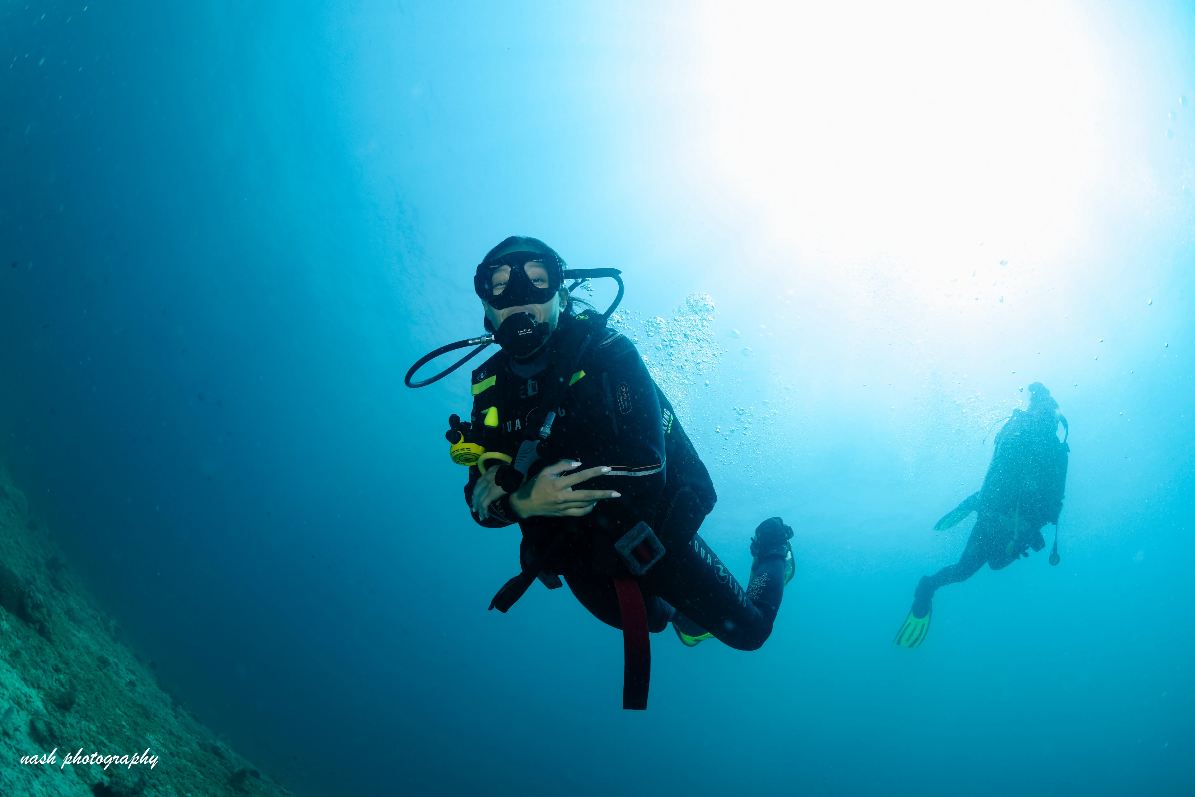 Diver descending in blue water with a buddy behind