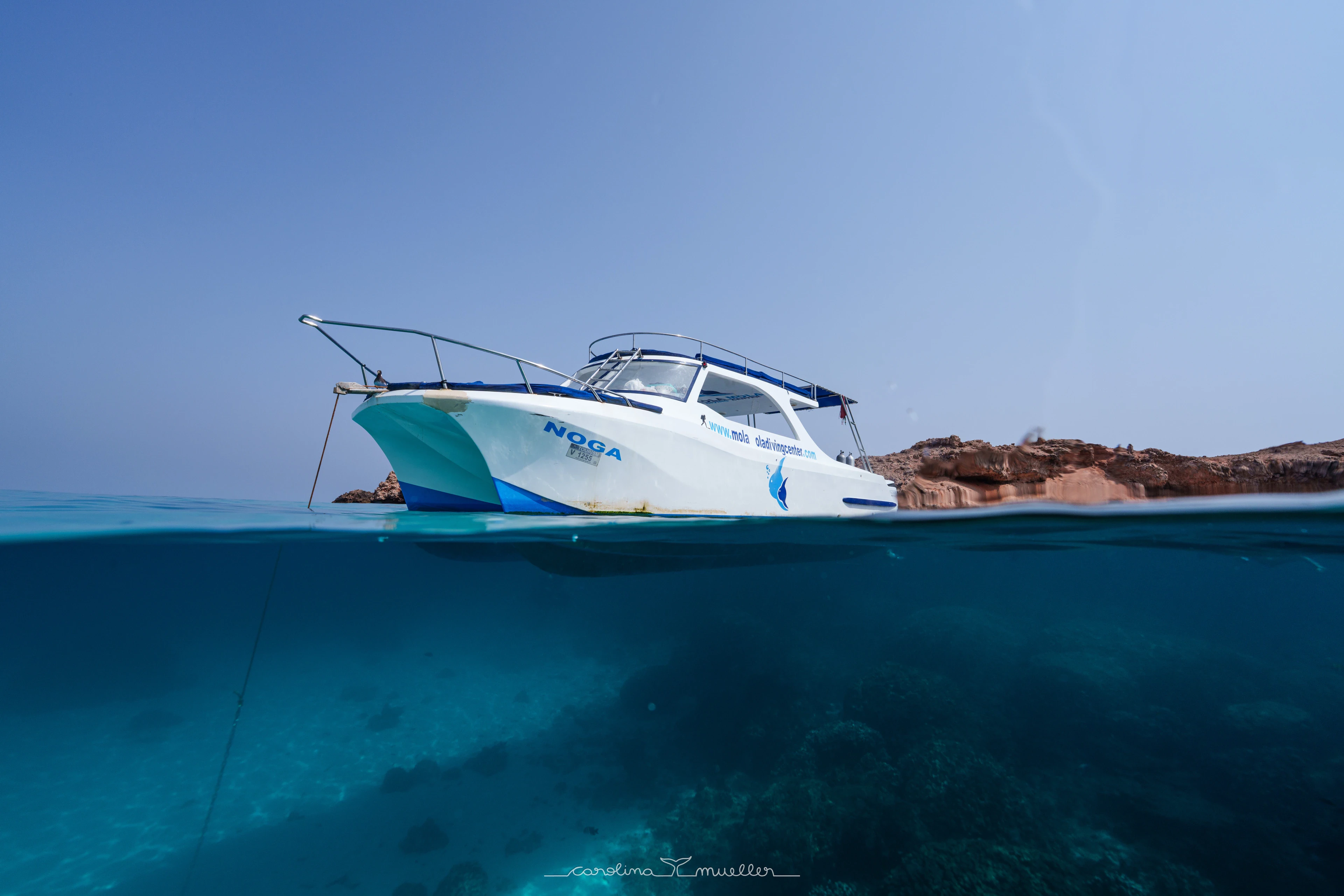 MolaMola boat above clear water and reef, half underwater view